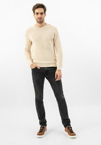 Svetle béžový žebrovaný pletený svetr v kombinaci s tmavými džíny a hnědými teniskami. Tento outfit má jednoduchý design s kulatým výstřihem a přiléhavým střihem.