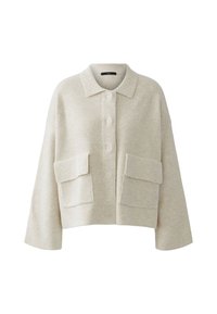 Afgeknot beige gebreid shirt met een kraag, knoopsluiting en twee grote voorzakken. Zachte textuur, brede mouwen en een relaxte pasvorm.