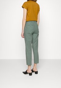 Groene geruite broeken met een getailleerde pasvorm, voorzien van een middelhoge taille en achterzakken. Gekleed met een roestkleurige cropped top en zwart blokhak schoenen.