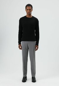 Pull en maille côtelée noire avec un col rond, associé à un pantalon tailleur gris clair et des chaussures en cuir noires.
