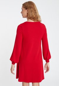 Rotes Strickkleid mit langen, puffigen Ärmeln. Hat einen runden Ausschnitt und eine lockere Passform, die bis zur Mitte des Oberschenkels reicht. Glatte Textur.