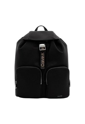 Sac à dos en cuir noir avec deux poches avant zippées, rabat supérieur avec une boucle argentée et le logo Calvin Klein sur la sangle et la poche.