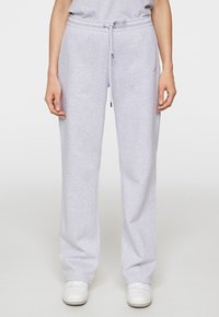 Lichtgrijze sweatpants van zacht materiaal, met een elastische tailleband met trekkoord en een losse pasvorm, gecombineerd met witte sneakers.