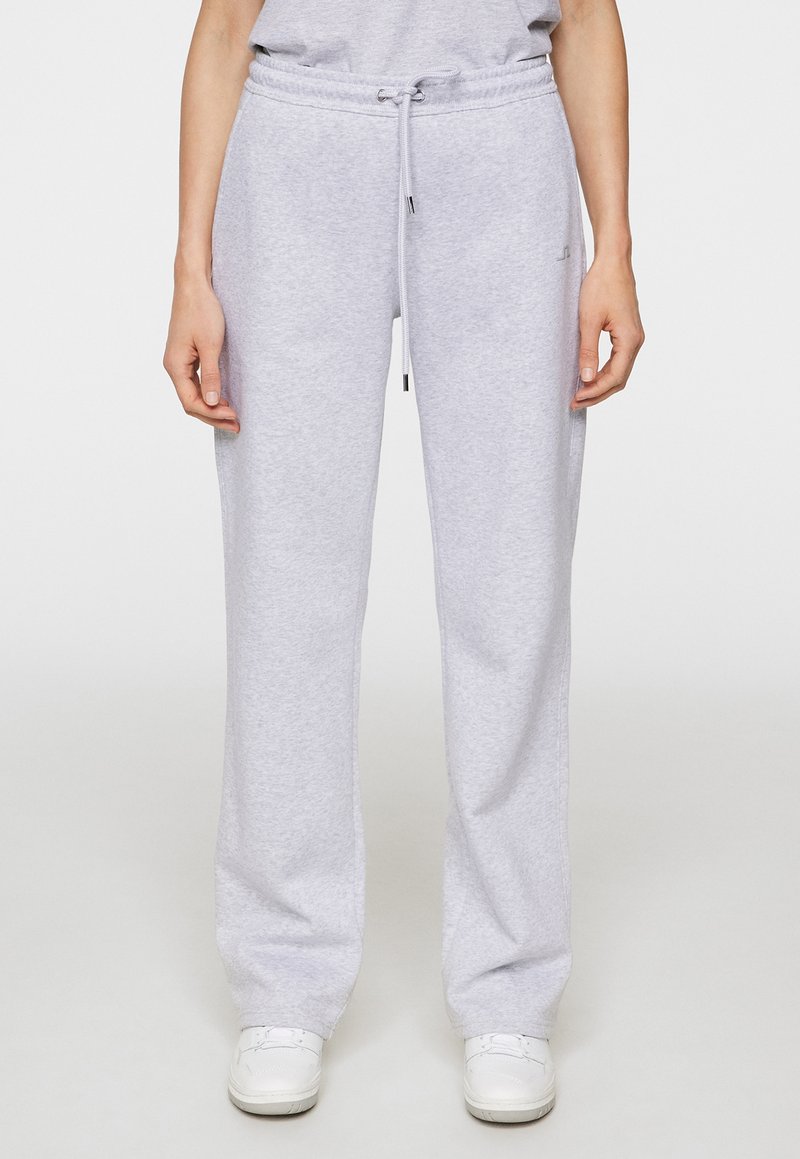 Lichtgrijze sweatpants van zacht materiaal, met een elastische tailleband met trekkoord en een losse pasvorm, gecombineerd met witte sneakers.
