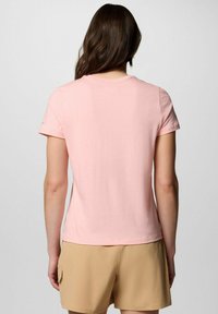 T-shirt rosa chiaro a maniche corte con colletto rotondo e tessuto morbido, abbinata a pantaloni corti beige, vista da dietro.