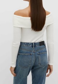 Biała, prążkowana bluzka bez ramiączek, połączona z niebieskimi dżinsami z wysokim stanem, z czarną skórzaną metką na tylnym pasie.