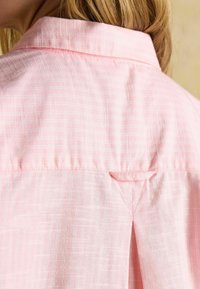 Svetloružová košeľa s jemným kockovaným vzorom, s klasickým golierom a trojuholníkovým sklom vzadu. Textúrovaná tkanina.