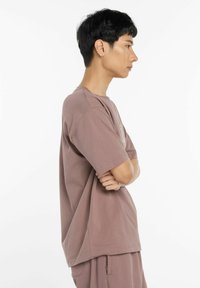 Vaalean liila puuvillapaita, jossa on rento istuvuus, lyhyet hihat ja pyöreä kaula-aukko, esiteltynä mallilla, joka seisoo kylki edellä kädet ristissä.