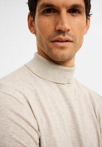 Helle beige Rollkragenpullover aus weichem Strickstoff. Verfügt über einen gerippten Kragen und eine subtile Textur, die eng am Hals anliegt.
