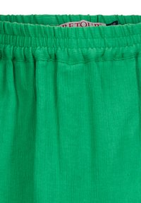 Grüner, strukturierter Stoff mit einem gerafften, elastischen Bund, der ein leichtes und schwingendes Design zeigt. Etiketten kennzeichnen die Marke und Pflegeanweisungen.