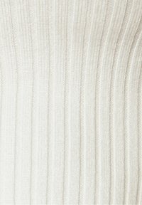 Gros plan sur un tissu en maille côtelée blanche montrant des rayures texturées verticales et des détails de couture fines.