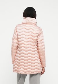Jachetă îmblănită de culoare roz deschis, cu un design cusut în valuri, guler înalt și mâneci lungi. Textură netedă cu un finisaj lucios.