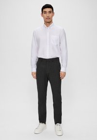 Chemise blanche à boutons avec une poche poitrine, associée à un pantalon à carreaux sombres et des baskets blanches. Design simple et coupe ajustée.