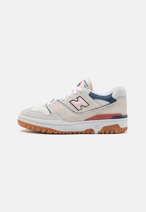 Zapatilla New Balance 550 en ante beige y malla con acentos en azul marino y rojo, cordones blancos y suela de goma color caramelo.