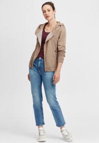 Brun zip-up hettegenser med grå innvendig fôr, kombinert med en burgunder topp og lyseblå straight-leg jeans. Kremfargede sneakers fullfører antrekket.