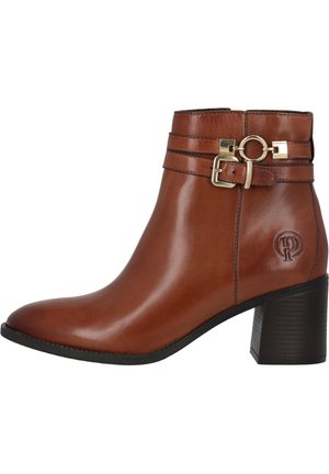 Bottine en cuir marron avec un bout arrondi, deux sangles décoratives, des accents en métal doré et un talon bloc texturé. Logo embossé sur le côté.
