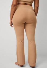 Nude flared leggings lavet af strækbart stof med en glat tekstur. Har en høj talje og sømdetaljer langs ryggen.