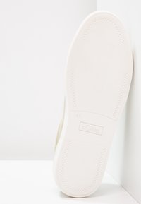 Světlý béžový tenisk s bílou gumovou podrážkou. Má strukturovaný povrch a jemné značení na podrážce, označená velikost 37.