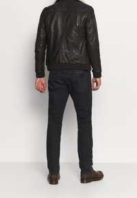 Sort læderjakke med pelskrave, ribbede håndled og kant. Mørke denimjeans og brune læderstøvler fuldender outfittet.