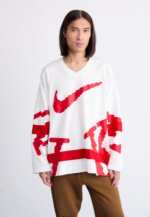 White, long-sleeve jersey with a V-neck and oversized fit, featuring a large red Nike logo and abstract red graphics on the sleeves and body.