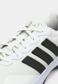 Fehér sportcipő légáteresztő hálós felsőrésszel, három fekete texturált csíkkal, valamint kontrasztos fehér díszítésekkel a nyelven és a fűzőlyukaknál.