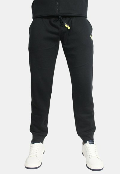 Pantaloni della tuta neri realizzati in un tessuto morbido, dotati di vita con coulisse e tasche laterali, abbinati a sneakers bianche.