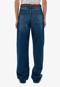 Denim jeans met een losse fit, donkerblauwe kleur en twee achterzakken. Voorzien van een gevlochten bruine leren riem om de taille.