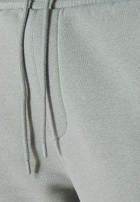 Lichtgrijze sweatpants van zachte stof, met een trekkoordsluiting en een zijzak. De textuur is glad met een casual ontwerp.