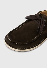 Brown suede shoe with a rounded toe, white stitching details, and dark brown laces. Features a cushioned insole and a textured outsole.