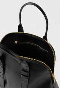 Μαύρη δερμάτινη τσάντα με χρυσό φερμουάρ ανοιχτή, δείχνοντας την εσωτερική τσέπη με φερμουάρ και τις διπλές λαβές με λεπτομέρειες από αγκράφες.