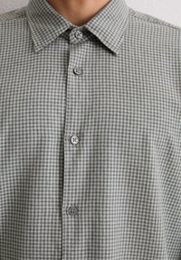 Gingham-musteriertes Hemd in Grau und Weiß. Verfügt über einen spitzen Kragen, sechs Knöpfe und einen weichen, strukturierten Stoff.
