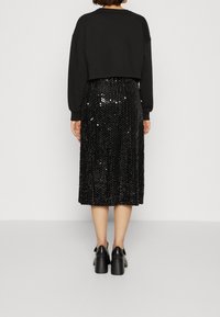 Sweat-shirt noir raccourci associé à une jupe midi noire à sequins. La jupe présente des motifs verticaux en sequins et une taille ajustée. Chaussures noires à talons carrés.