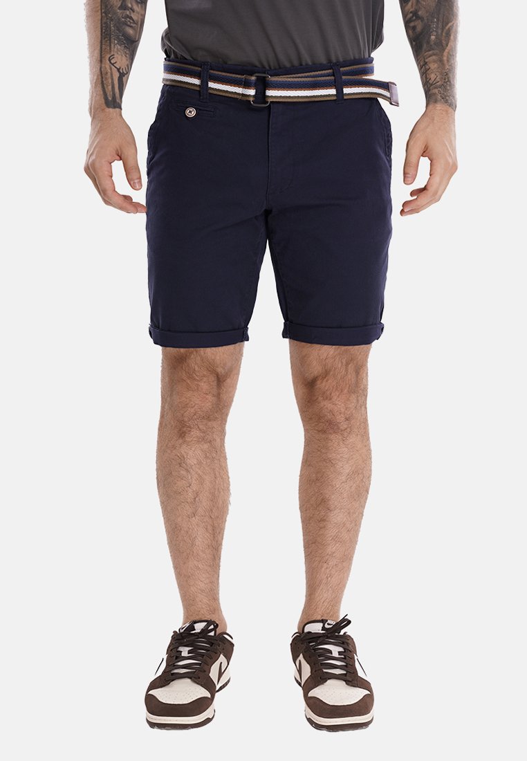 Pantaloni corta di cotone blu navy con orlo arrotolato, dotati di una tasca frontale e di una cintura a righe in blu navy, marrone e crema. Inclusi sneakers marroni e bianche.