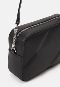 Czarna skórzana torebka o geometrycznym wzorze, z metalowym zamkiem błyskawicznym i detalem łańcucha. Kompaktowy prostokątny kształt z gładką teksturą.
