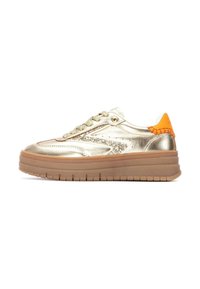 Zapatillas metálicas doradas con un acabado brillante, acentos texturizados, talón naranja y suela de goma gruesa. Presentan un cierre con cordones y un diseño de corte bajo.