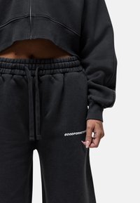 Zwarte cropped sweatshirt en sweatpants set gemaakt van pluizige stof. Heeft een tailleband met trekkoord en logo-details op de broek. Soepele textuur.