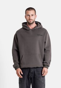 Mörkgrå pull-over-hoodie i mjukt material, med känguruficka, justerbar dragkedja på huvan och broderad logotyp på bröstet.