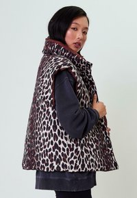 Pufová vesta s leopardím vzorom, vysokým golierom, bez rukávov a kontrastnými burgundskými akcentmi. Vyrobená z textúrovanej tkaniny.