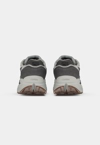 Chaussures d'extérieur grises et blanches avec une tige en suède texturé et en mesh, dotées de semelles en caoutchouc Vibram et d'accents distincts au niveau du talon.