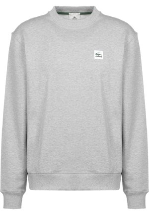 Sudadera gris de manga larga con cuello redondo, puños y bajo acanalados, con un pequeño parche con el logo de Lacoste en el pecho izquierdo.