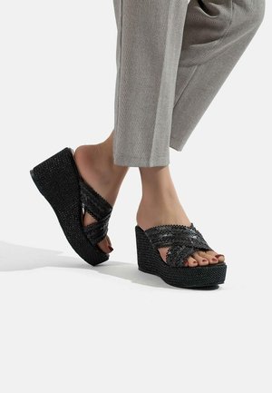 Sandales compensées noires en matière tissée, avec des brides croisées et une semelle texturée. Design à bout ouvert avec des détails d'accent sur les brides.