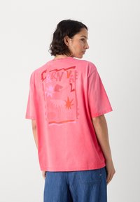Rosa oversized t-skjorte med korte ermer, med en fargerik grafisk design på baksiden, inkludert stjerner og abstrakte former.