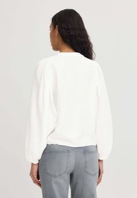 Bílý dlouhý rukáv top s vycpanými rameny a strukturovanou látkou, v kombinaci se šedými džíny s zadními kapsami a slim fit střihem.
