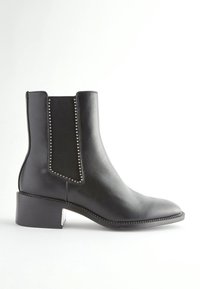 Bottine en cuir noir avec talon carré bas, panneau latéral élastique et petits clous argentés le long des bords du panneau.