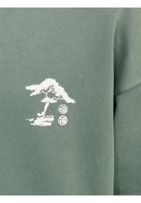 Oliivinvihreä collegepaita, jossa on valkoinen puu- ja tekstikuvio. Materiaali on pehmeä ja siinä on teksturoitu pinta. Muotoilussa on yksityiskohtaista koristelua.