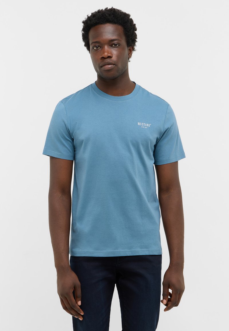 Koszulka z krótkim rękawem, okrągłym dekoltem w jasnoniebieskim kolorze, wykonana z bawełny, z małym białym logo po lewej stronie klatki piersiowej i luźnym krojem.