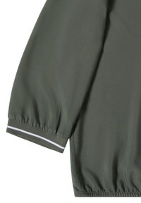 Manche d'une chemise à manches longues vert foncé avec un poignet élastique présentant une seule bande blanche horizontale près du bord.