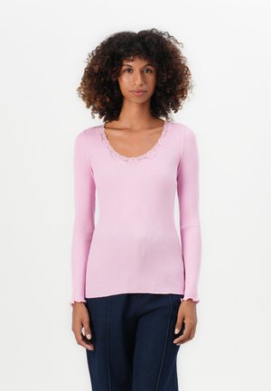Langærmet ribbet top i lys pink med en bølget blondeudskæring. Blød tekstur, tætsiddende design, med voluminøse manchetter og en lige kant.