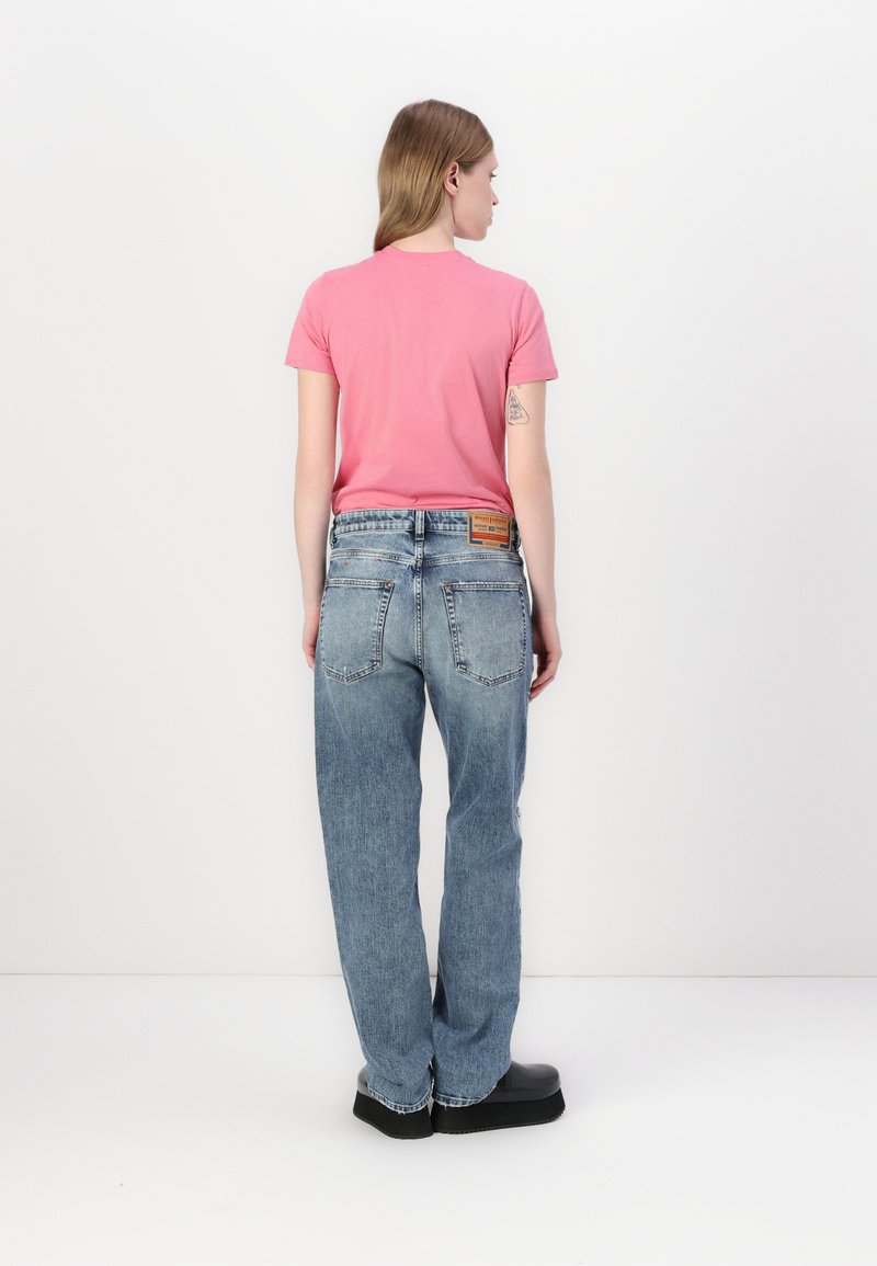 Rosa Kurzarm-T-Shirt kombiniert mit hoch sitzenden, locker sitzenden hellblauen Jeans, die ein Patchlabel auf der Rückseite haben, und schwarzen Plateaustiefeln.