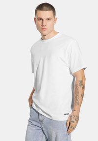 Biała koszulka z krótkim rękawem wykonana z bawełny, z okrągłym dekoltem i małym logo na dole. Teksturowana tkanina. Szorty z jasnego denimu.